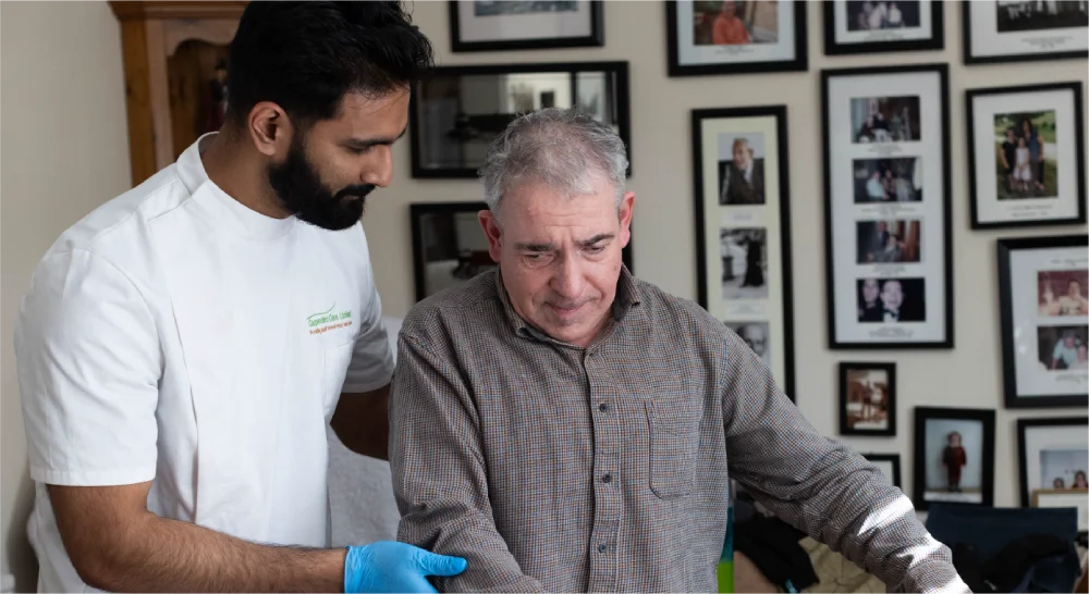 Caregiver assists an elderly man seated indoors.