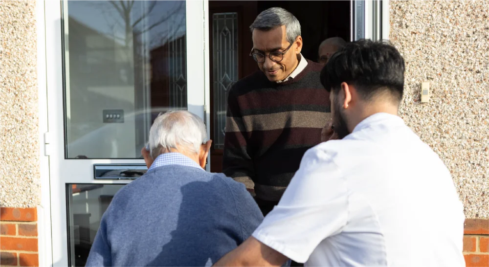 Three men stand at a doorway in bright sunlight.
