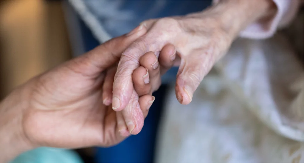 A caregiver gently holds an elderly person's hand.